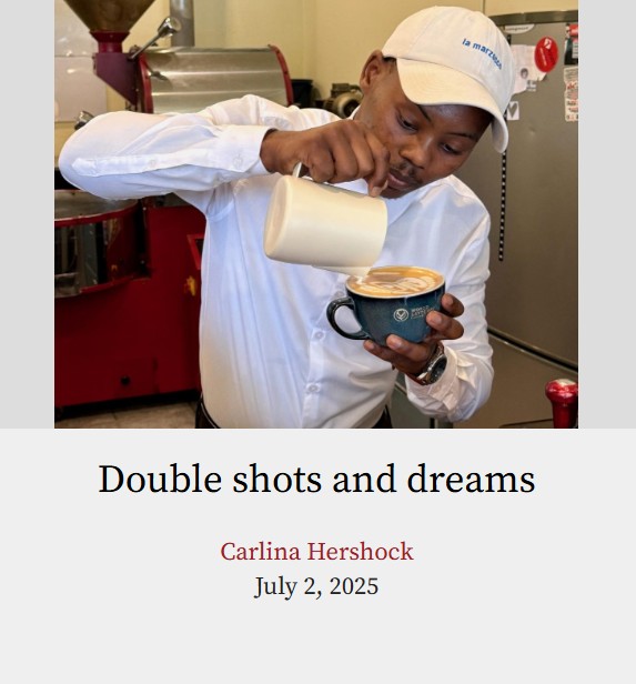 A photo of an African American man pouring concentrated milk onto a cup of coffee while creating a design. The man is wearing a white blouse with a white hat on his head. He is staring down at the cup of coffee, concentrating on his work.
